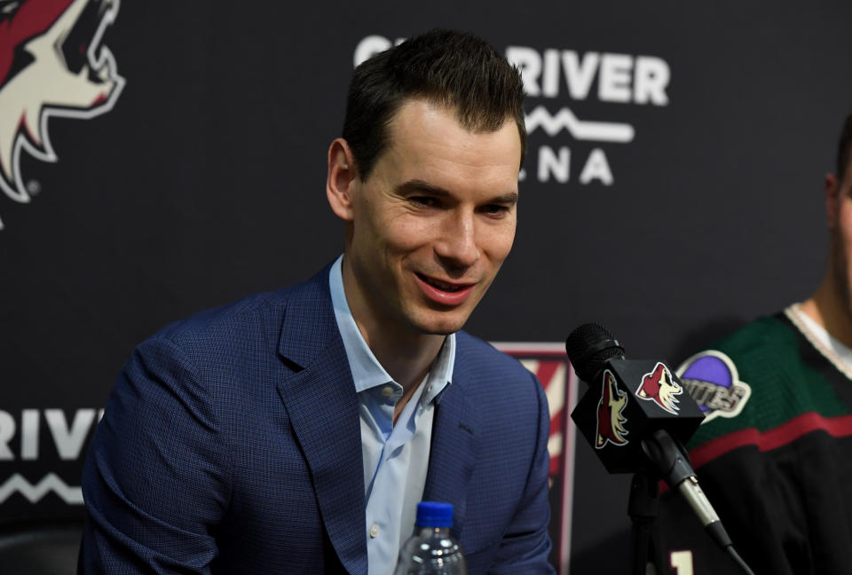 John Chayka smiles at a podium answering questions. 