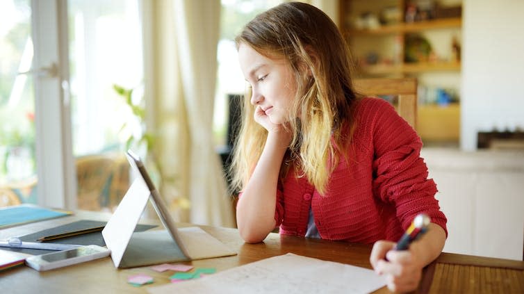 A preteen girl does schoolwork with a tablet.