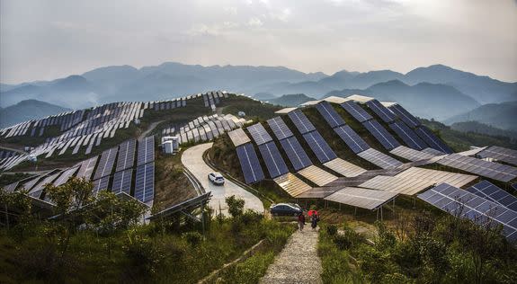 People walk past solar panels at a photovoltaic power station southeastern China's Fujian province, Aug. 21, 2016.