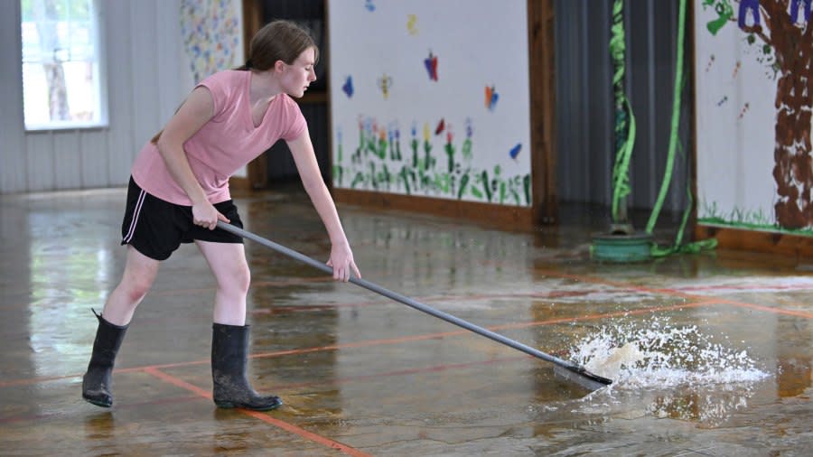 Ashley Joiner, 17, uses a squeegee broom to push water out of the fellowship hall at the Christian Church in Flippin, Ark., after it flooded on Wednesday, July 17, 2024. (Staci Vandagriff/Arkansas Democrat-Gazette via AP)