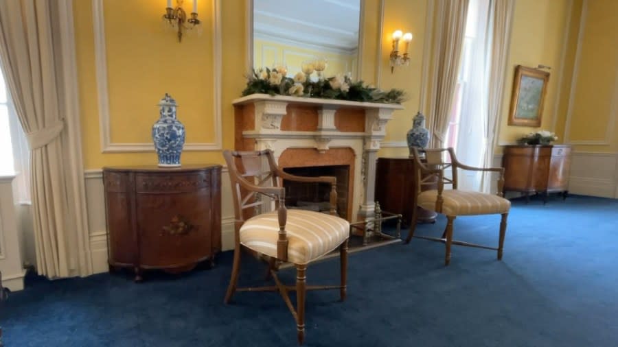 A photo of the "Best Room" which has canary yellow on the walls, white trim and royal blue carpet. The room is decorated with wooden furniture, landscape paintings and ornate ceramics.