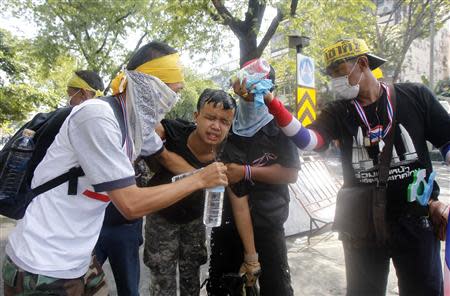 Anti-government protesters assist an injured protester after riot policemen threw a teargas canister during clashes with police near the metropolitan police headquarters in Bangkok December 1, 2013. REUTERS/Chaiwat Subprasom