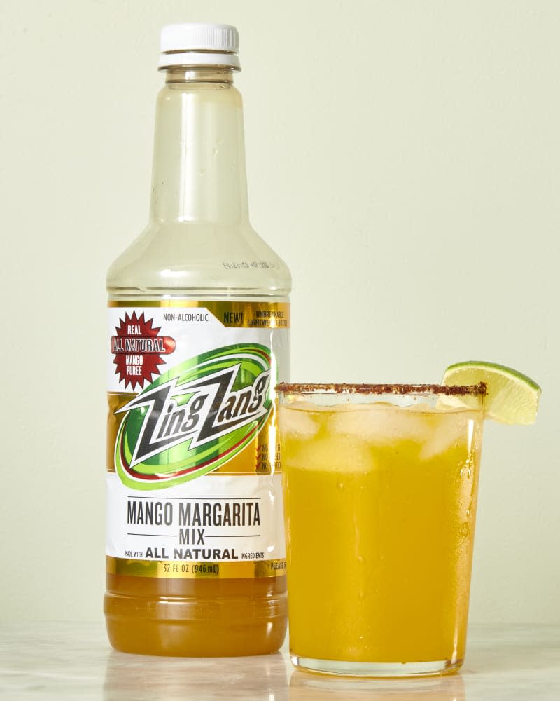 photo of Zing Zang Mango Margarita mix bottle with a mixed drink next to it on a marble surface with a light green background