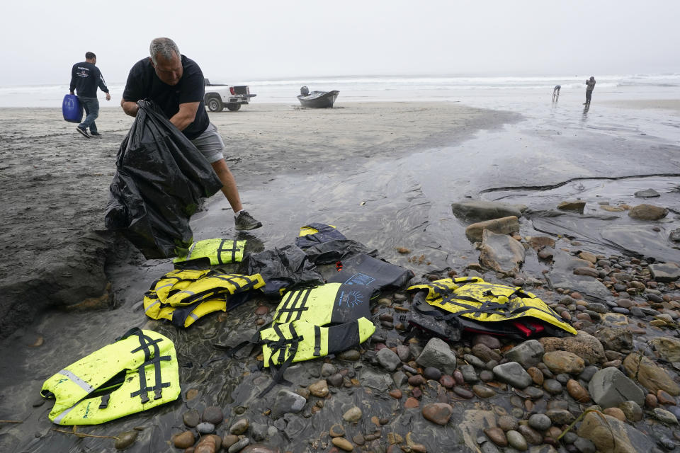 ARCHIVO - El socorrista Robert Butler recoge en una bolsa chalecos salvavidas que se encuentran cerca de uno de dos botes que se volcaron cuando transportaban a migrnates en aguas poco profundas pero turbulentas frente a Blacks Beach, en la costa de San Diego, el 12 de marzo de 2023. (AP Foto/Gregory Bull, Archivo)