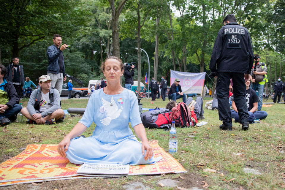 A woman is sitting with other supporters of the initiative "Querdenken 711" in Berlin's Tiergarten not far from the Federal Chancellery, Friday, Aug. 28, 2020. Police in Berlin have requested thousands of reinforcements from other parts of Germany to cope with planned protests at the weekend by people opposed to coronavirus restrictions. (Christoph Soeder/dpa via AP)