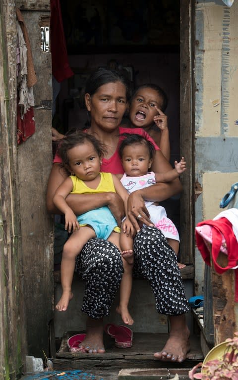 Maryann Barrios, aged two (in the yellow vest, held by her mother Mylene) is stunted and wasted. Her siblings – also pictured sitting in the doorway of their house – are also affected by malnutrition, but to a lesser extent. The family live in an illegal settlement called Market Three near the docks, in North Bay Boulevard North, Metro Manila. - Credit: Simon Townsley