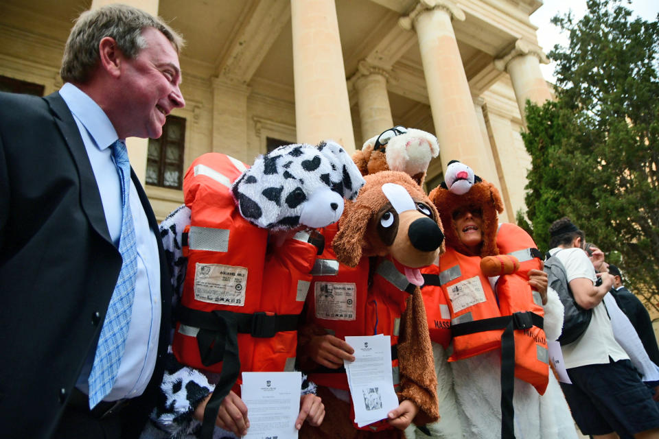 Claus-Peter Reisch, German captain of Lifeline, a private ship that rescued migrants, center, shares a laugh with Mission Lifeline activists dressed as dogs outside the courthouse ahead of a hearing in Valletta, Malta, Tuesday, Oct. 2, 2018. Reisch is accused of using the ship in Maltese waters without proper registration or license after rescuing 234 migrants early this summer off Libyan waters and then heading to Malta after Italy refused entrance to the ship. (AP Photo/Jonathan Borg)