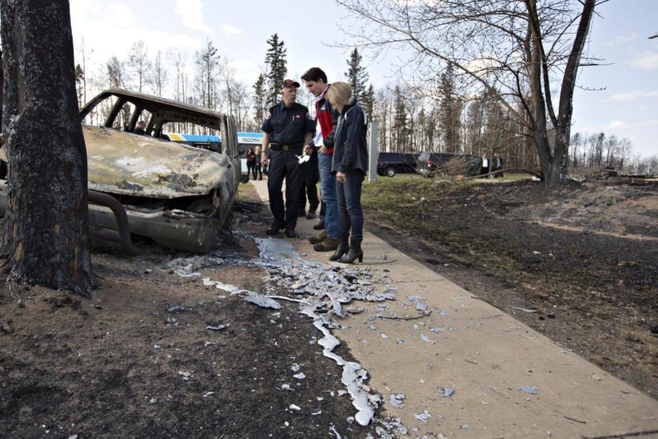 Fort McMurray Fire Chief Darby Allen, left to right, Prime Minister Justin Trudeau and Alberta Premier Rachel Notley look over a burnt out car during a visit to Fort McMurray, Alta., on Friday, May 13, 2016. THE CANADIAN PRESS/Jason Franson