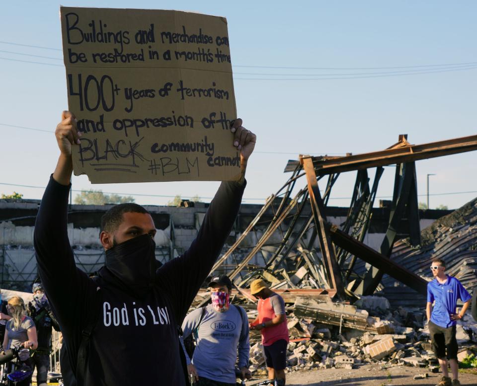 A protester holding a sign in front of a burned-out building Minneapolis during protests over the death of George Floyd on May 28, 2020. 