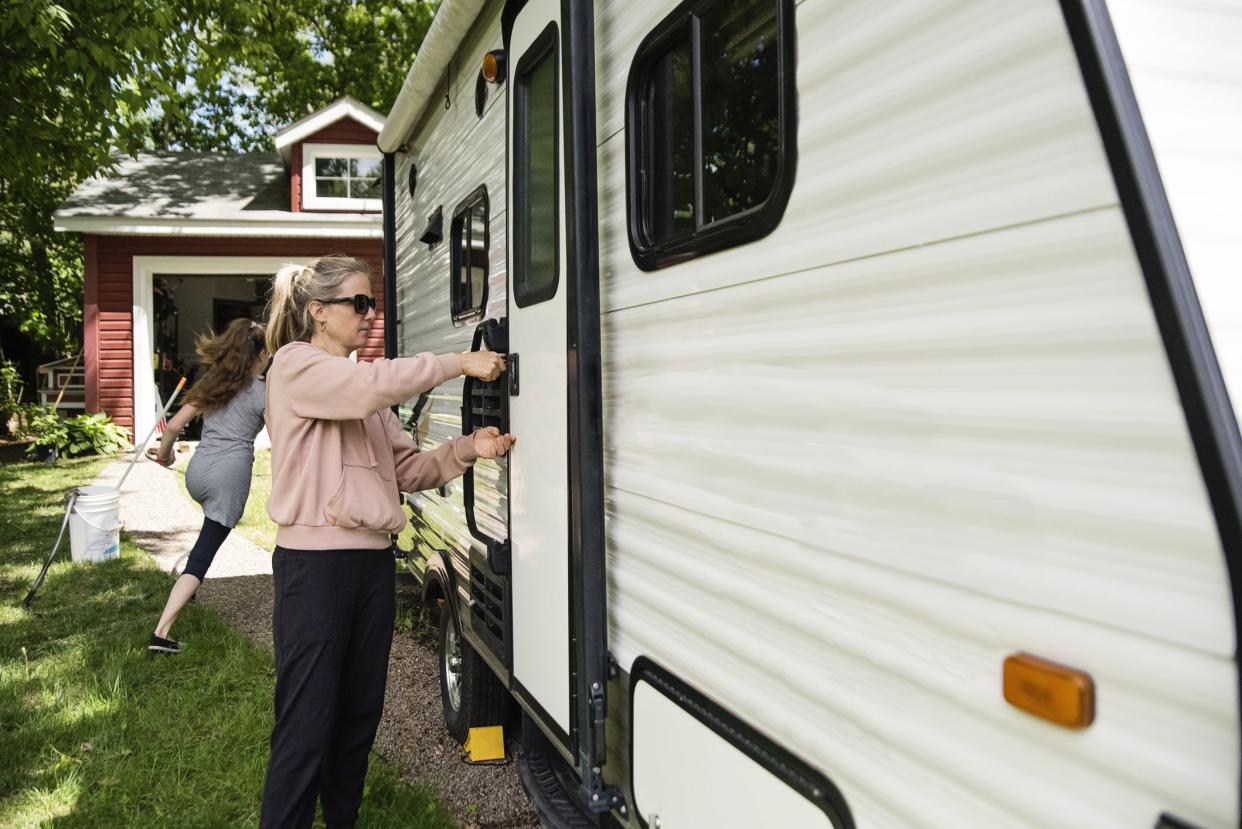 Mature woman getting RV ready to leave for summer vacations. She is locking the doors Daughter is running in the background. Horizontal waist up outdoors shot with copy space.