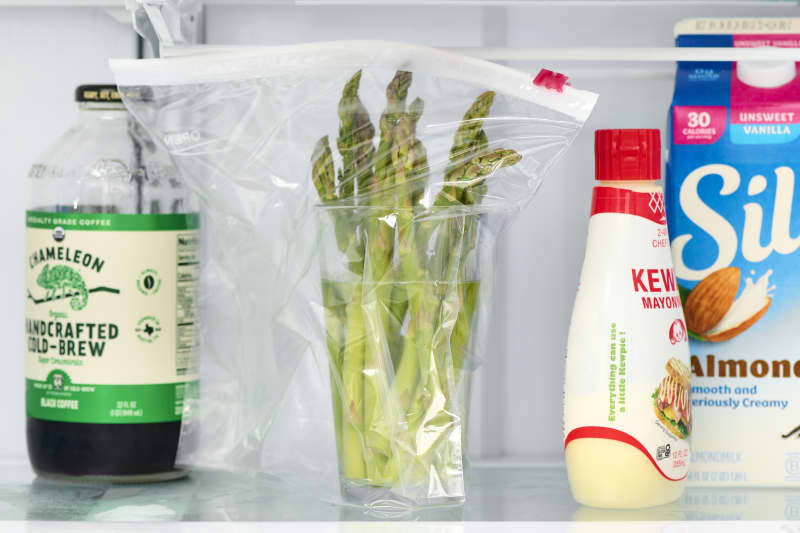 head on shot of asparagus in a glass of water, inside a plastic bag in the fridge.