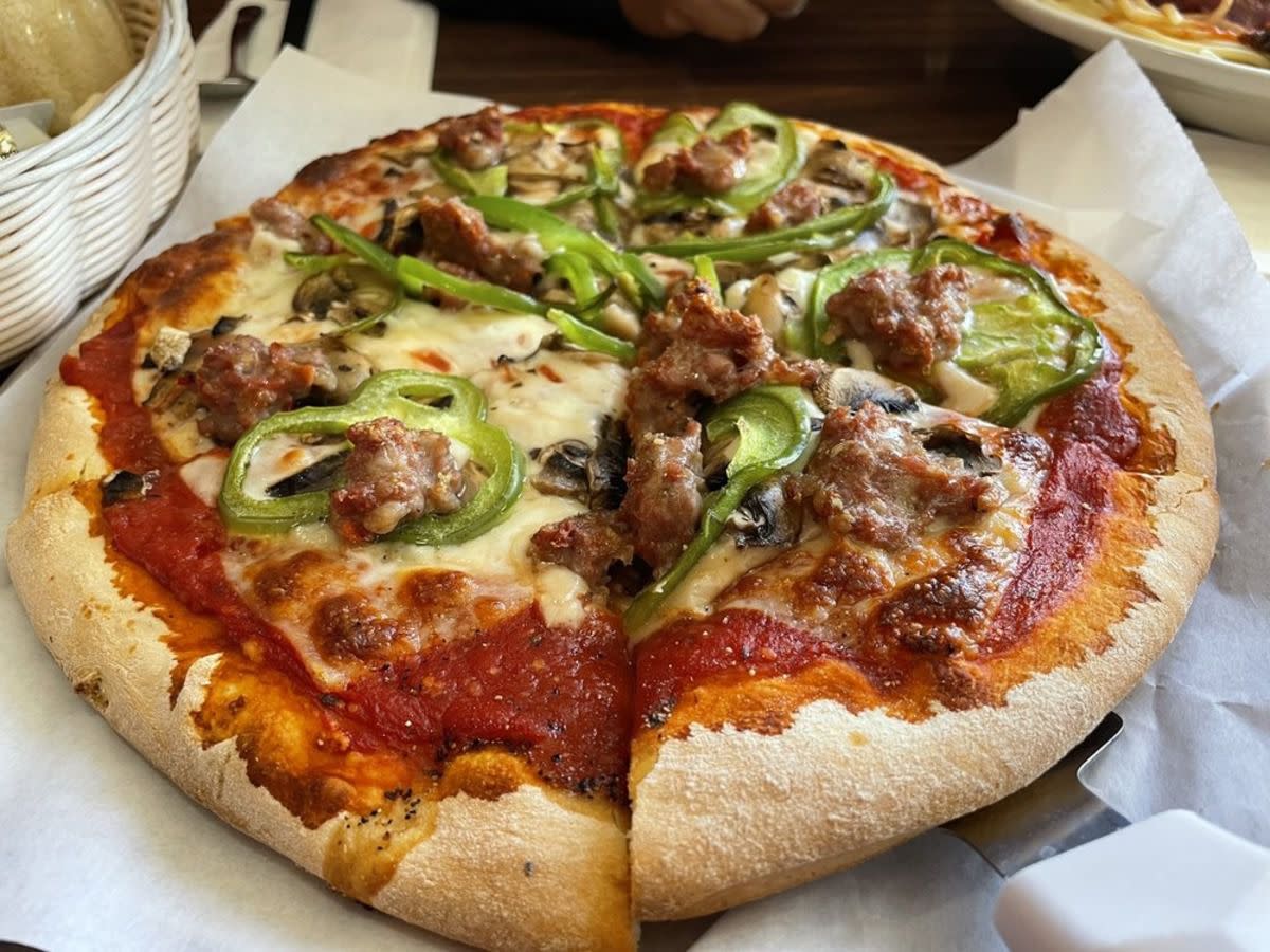 Sausage, bell pepper and mushroom pizza, Carl’s Pizza, Denver, Colorado, on white serving paper with a serving spatula, condiments and food along the top