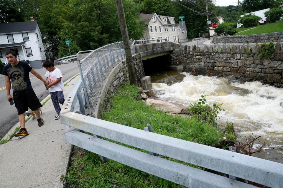 Pedestrians pass a local river whose heavy current flooded nearby Main Street, Monday, July 10, 2023, in Highland Falls, N.Y. Heavy rain has washed out roads and forced evacuations in the Northeast as more downpours were forecast throughout the day. One person in New York's Hudson Valley has drowned as she was trying to leave her home. (AP Photo/John Minchillo)
