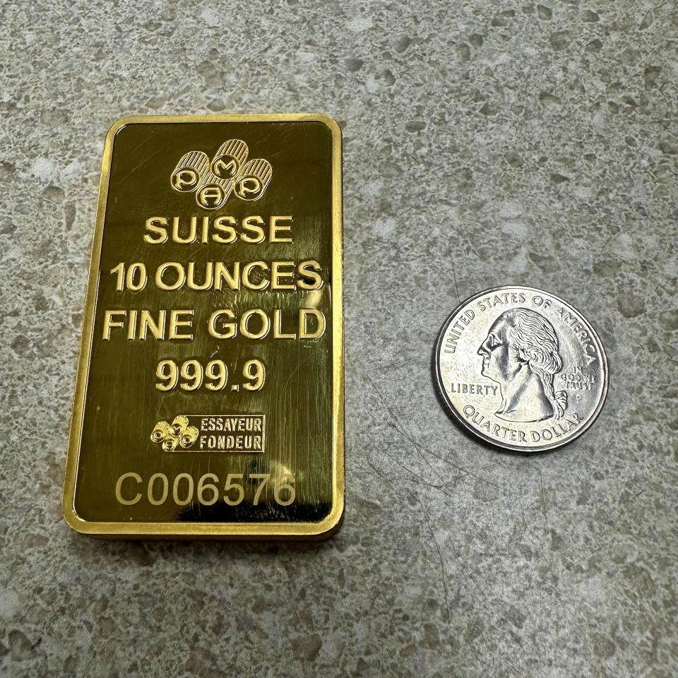 Gold bar labeled "SUISSE 10 OUNCES FINE GOLD 999.9" next to a U.S. quarter for size comparison