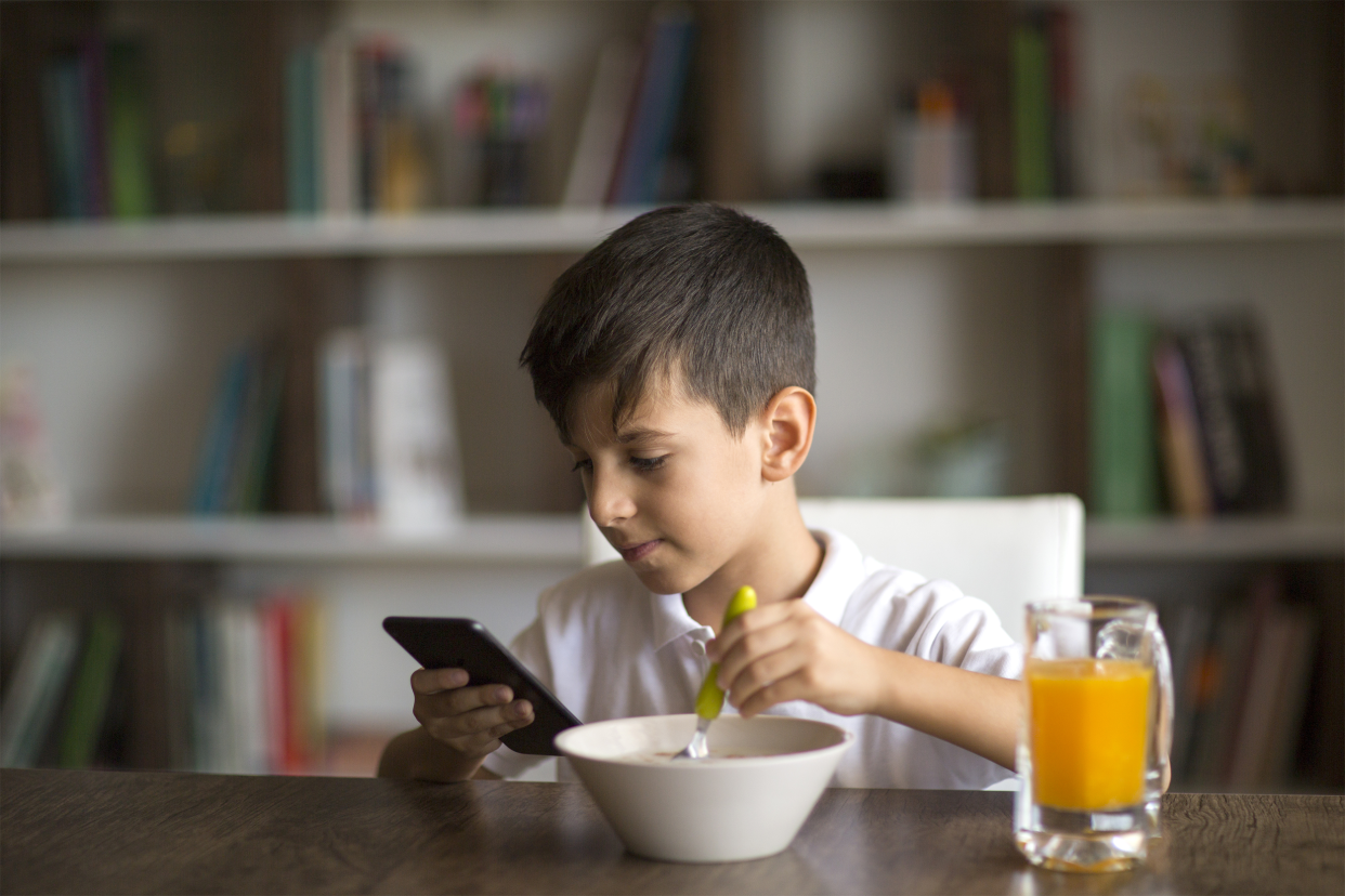 Boy on phone eating cereal