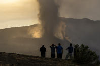 Residents watch from a hill as lava continues to flow from an erupted volcano, on the island of La Palma in the Canaries, Spain, Friday, Sept. 24, 2021. A volcano in Spain’s Canary Islands continues to produce explosions and spew out lava, five days after it erupted. Two rivers of lava continue to slide slowly down the hillside of La Palma on Friday. (AP Photo/Emilio Morenatti)