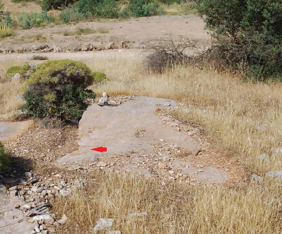 Patch of bedrock where the graffito is located (arrow); the earthen road is visible in the background (American Journal of Archaeology/Langdon et al)