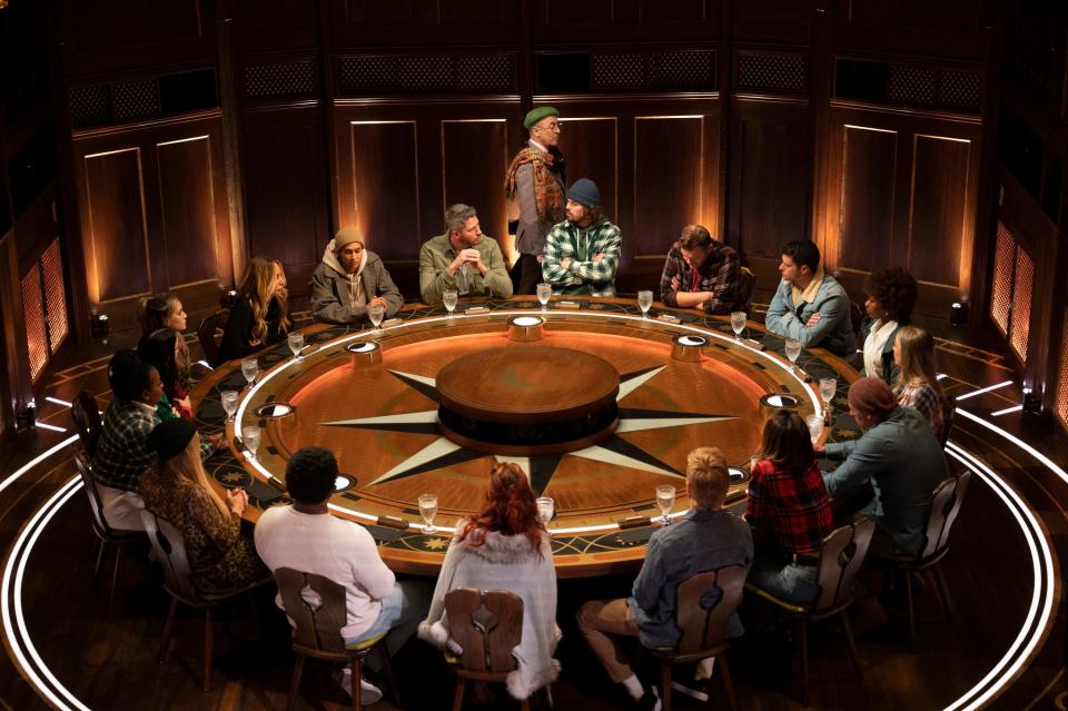 The Traitors season one round table, Alan Cumming walking around the contestants in a board room