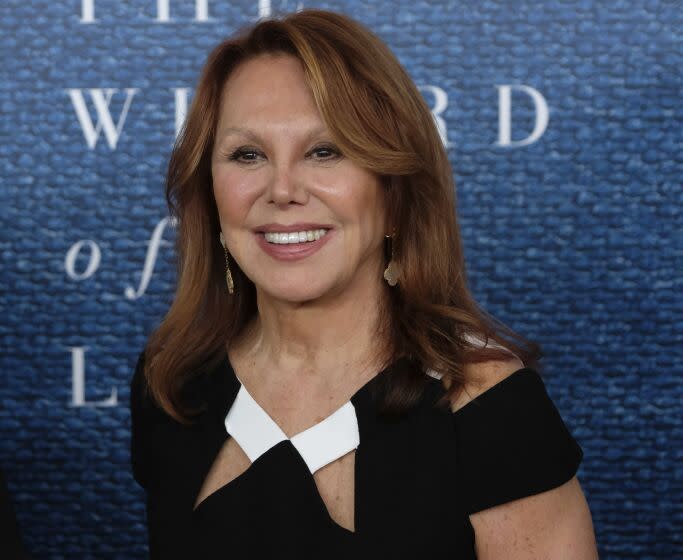 A long-haired woman in a black dress with white accents smiles as she arrives at the event