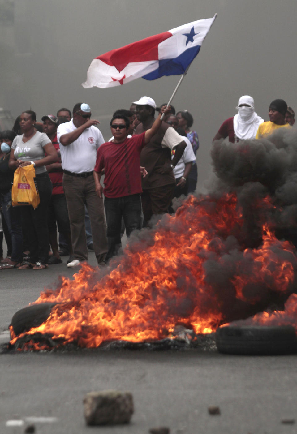 A demonstrator waves a Panamanian flag at a burning road block as he and others protest in Colon, Panama, Friday, Oct. 19, 2012. Demonstrators protested over a new law allowing the sale of state-owned land in the duty-free zone next to the Panama Canal. Protesters said the land is already being rented and it makes no sense to sell it. They said the government should instead raise the rent and invest the money in Colon, a poor and violent city. (AP Photo)
