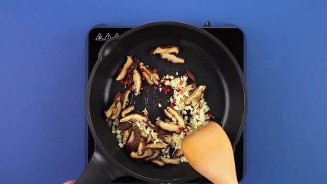 Frying mushrooms, garlic, and chili padi in a frying pan and wooden spatula