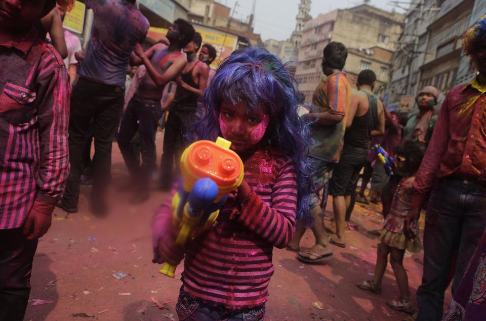 An Indian girl, face smeared with color, reacts to camera as she squirts water on others during celebrations marking Holi, the Hindu festival of colors, in Gauhati, India, Monday, March 17, 2014. The holiday, celebrated mainly in India and Nepal, marks the beginning of spring and the triumph of good over evil. (AP Photo/Anupam Nath)