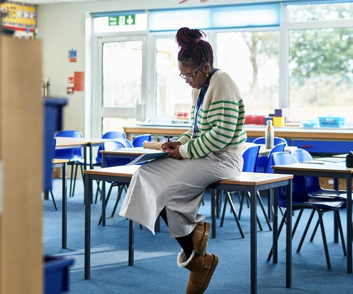 Teacher grading papers at a student's desk in an empty classroom