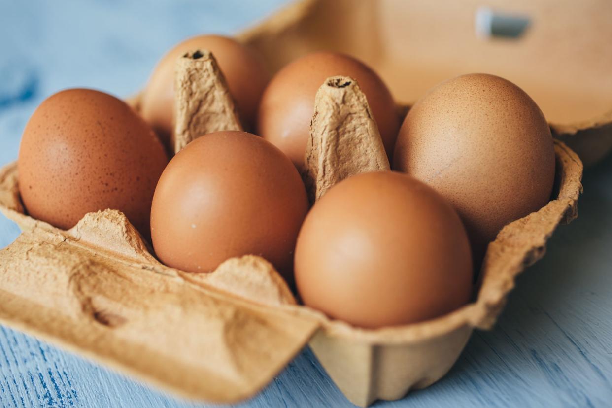 Closeup of 6 brown eggs in a brown half carton box on a blue wooden table