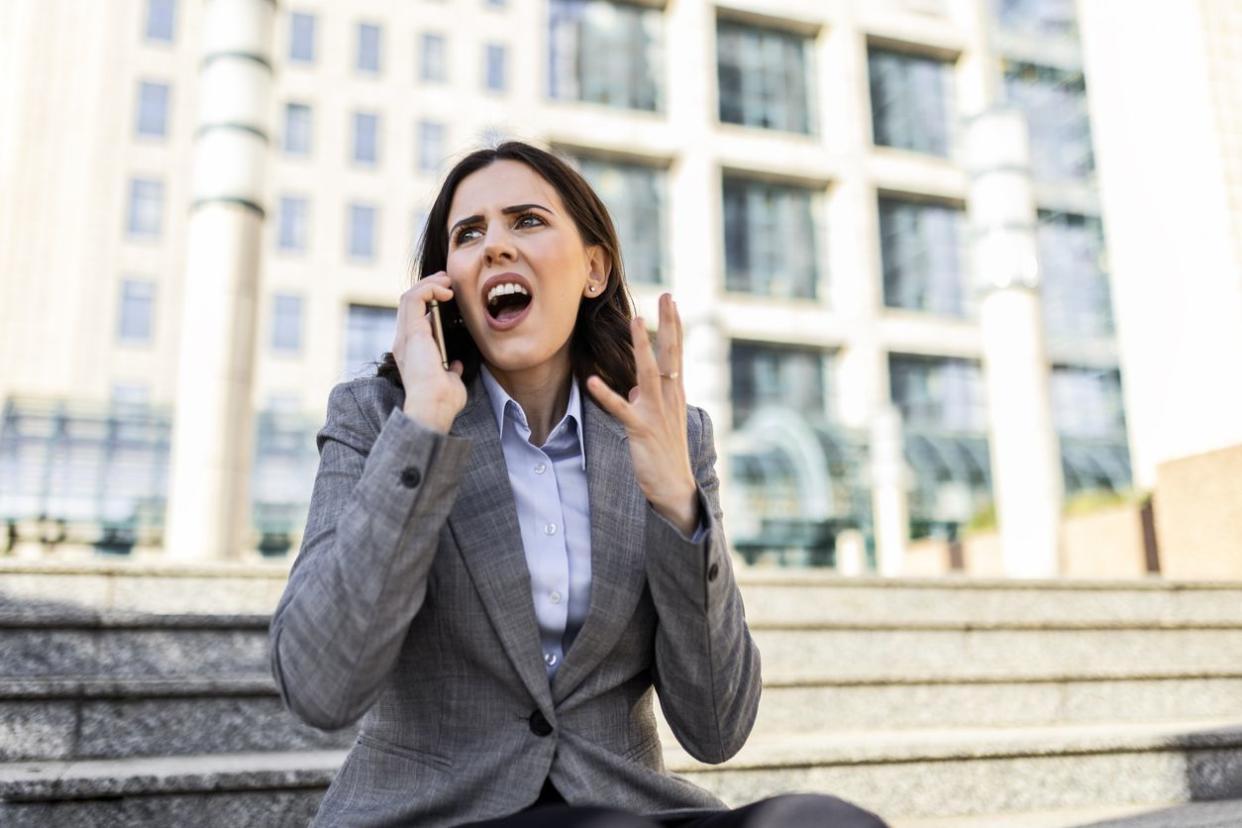 An angry female employee in a suit yelling on her phone.