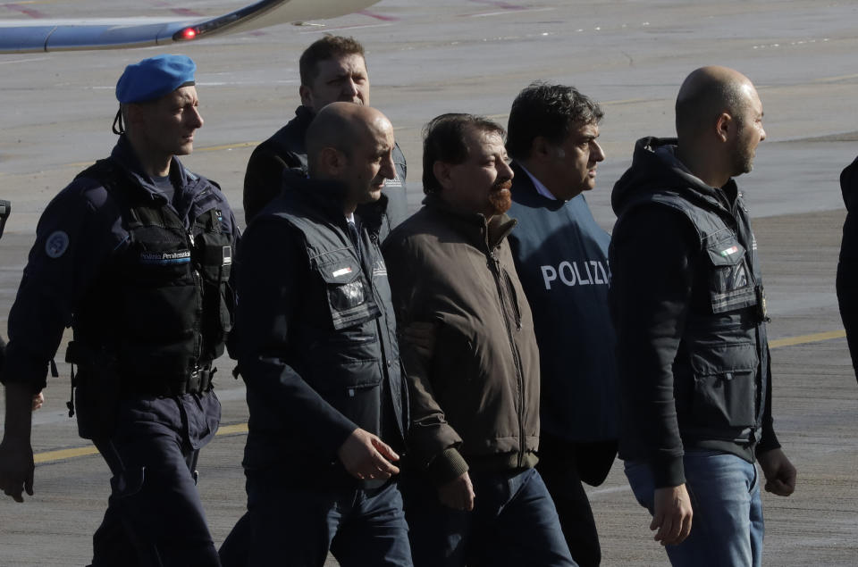 Italian fugitive Cesare Battisti, center, arrives at Ciampino military airport, in Rome, Monday, Jan. 14, 2019. Battisti a left-wing Italian militant who was convicted of murder three decades ago is heading home to serve a life sentence, after his life as a celebrity fugitive came to an abrupt end with his arrest in Bolivia by a team of Interpol agents. (AP Photo/Alessandra Tarantino)