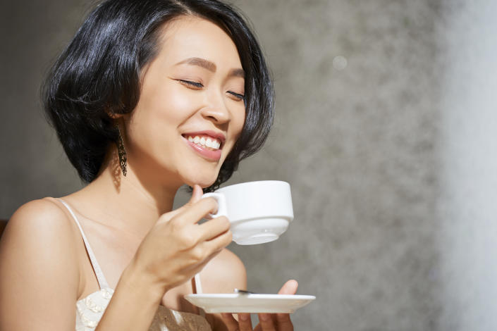 Face of joyful young Vietnamese woman enjoying cup of tasty tea at home