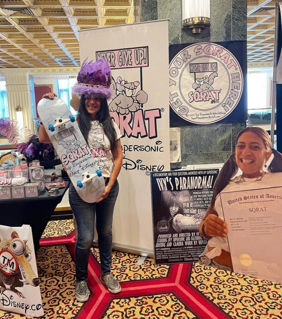 Ivy Supersonic holding a Sqrat skateboard and surrounded by merchandise
