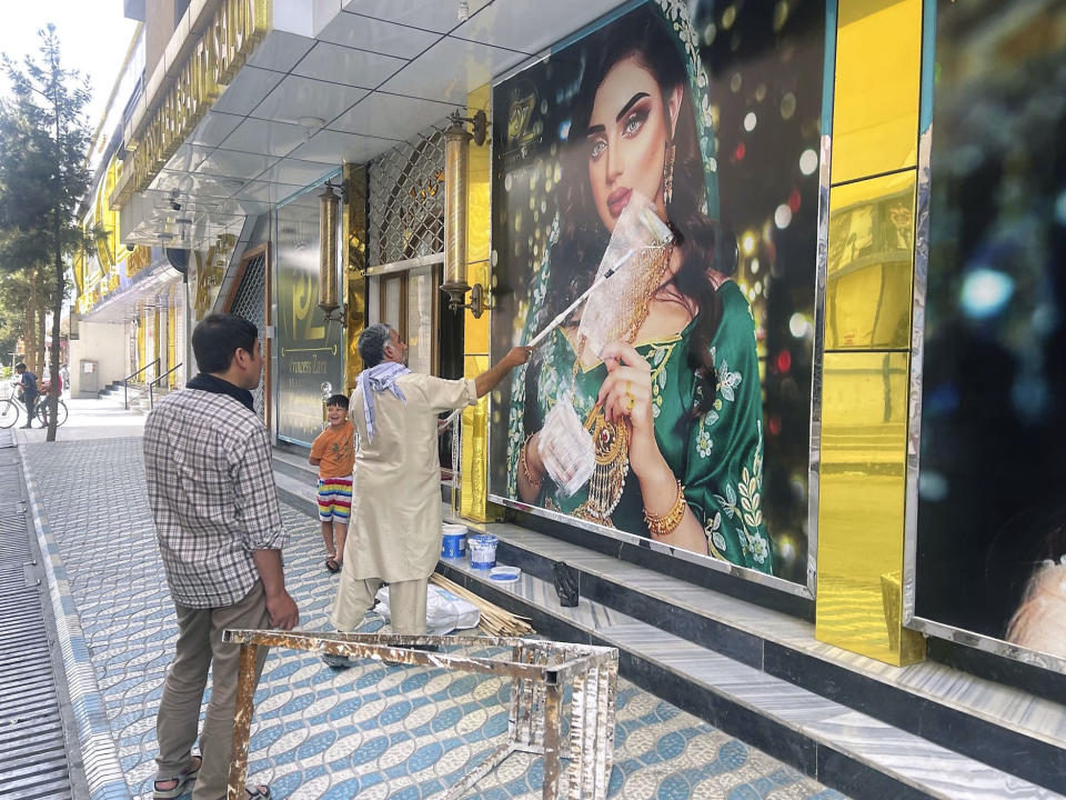A worker at a beauty salon paints over a large photo of a woman on the wall in Kabul following news that the Taliban swept into the Afghan capital