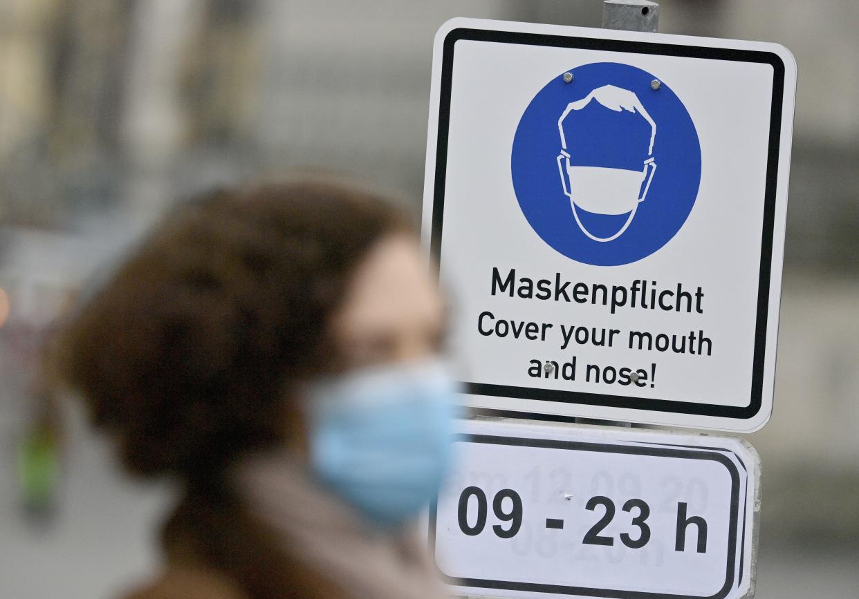 A woman, wearing a face mask, walks past a sign saying "Mask duty - Cover your mouth and nose!" in a pedestrian zone in the city center of Munich, Germany on Thursday, Oct. 15, 2020. German Chancellor Angela Merkel and Germany's 16 state governors agreed Wednesday night to tighten mask-wearing rules, make bars close early and limit the number of people who can gather in areas where coronavirus infection rates are high.