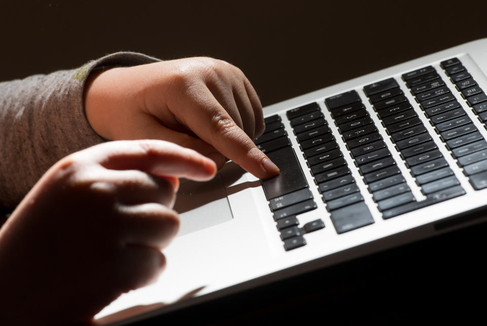 A child's hands on the keys of a laptop keyboard.