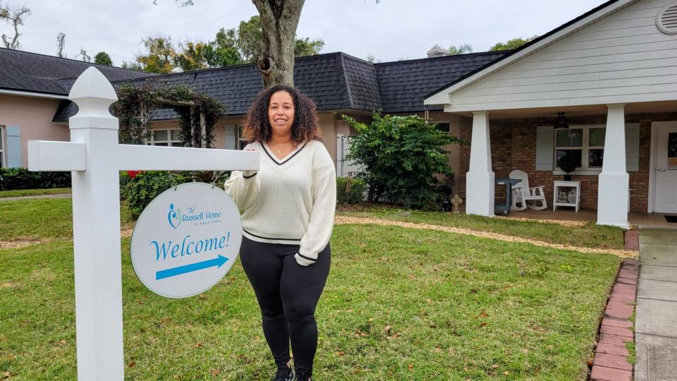 Amanda Brochu stands next to a sign outside The Russell Home.