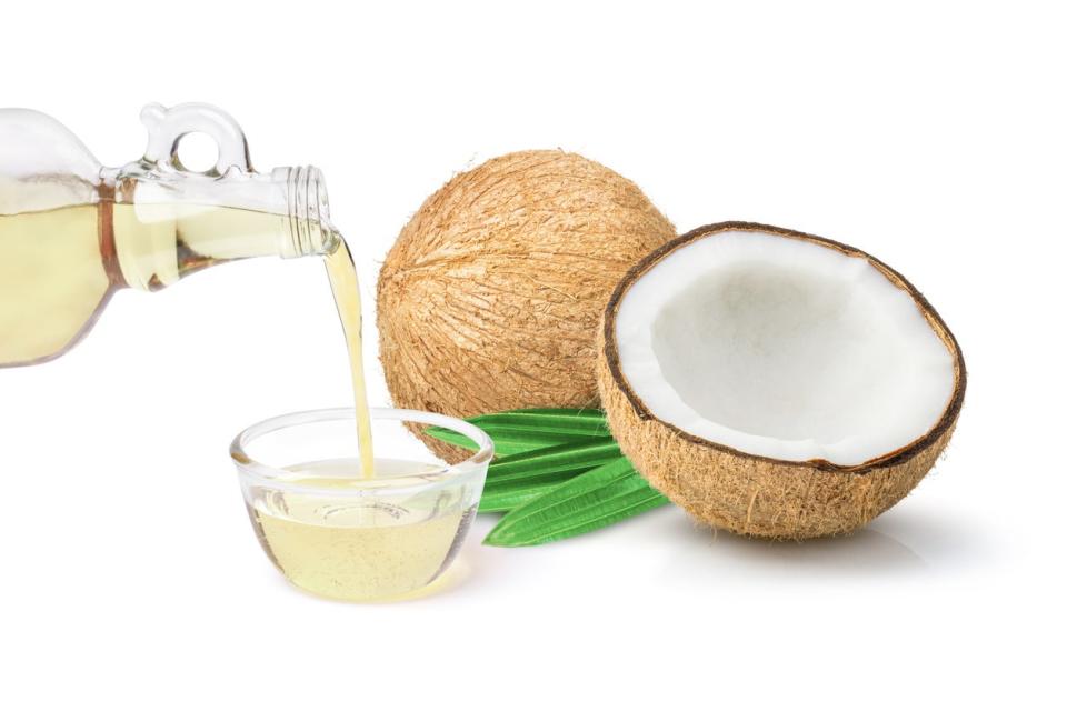 Coconut oil in glass bottle and coconut fruit with green leaves 