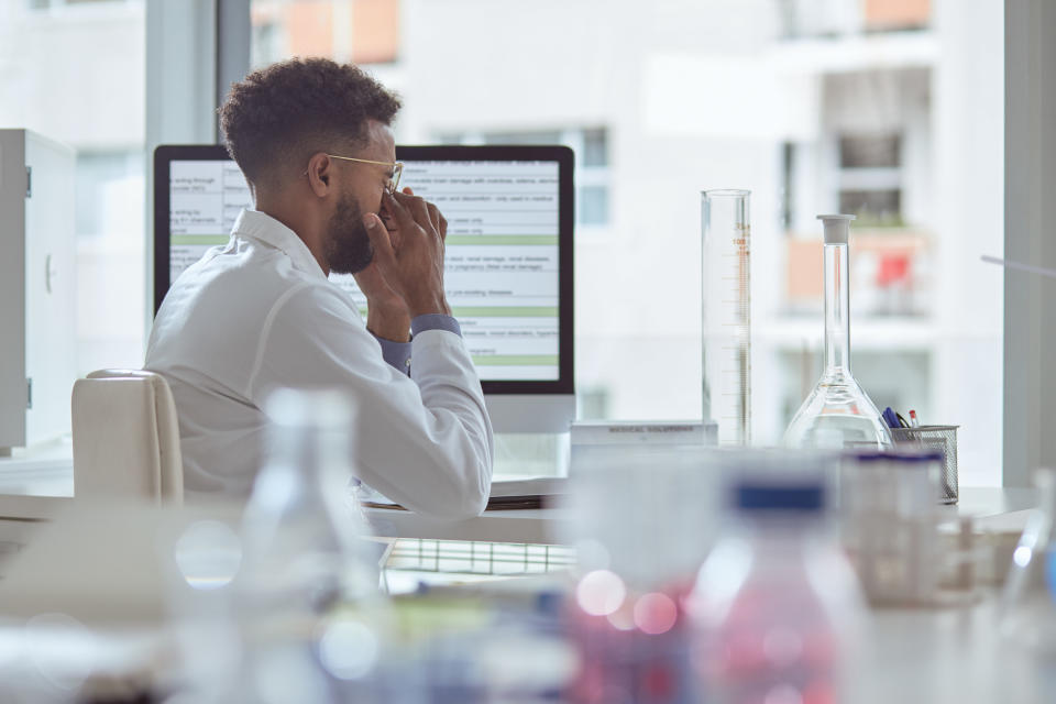 A scientist in a lab rubs his eyes as he becomes stressed at work