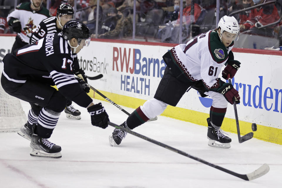 Arizona Coyotes defenseman Dysin Mayo (61) controls the puck in front of New Jersey Devils center Yegor Sharangovich (17) during the first period of an NHL hockey game Wednesday, Jan. 19, 2022, in Newark, N.J. (AP Photo/Adam Hunger)