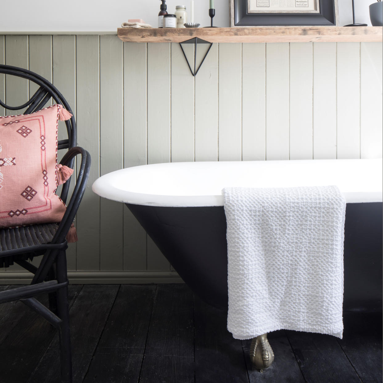  Black bathtub with towel hanging over, black rattan chair with cushion. 