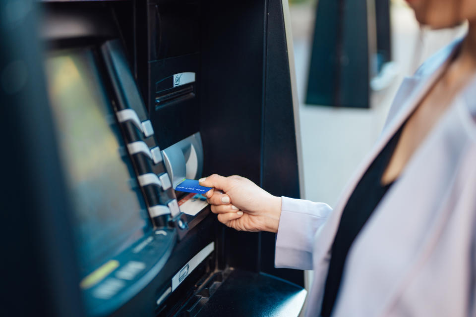 Young woman using automatic cash machine to withdraw money, make a bank transfer and check account balances. Privacy protection and mobile banking security concept.