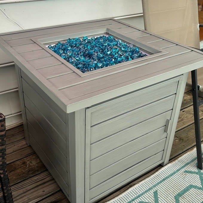 Outdoor gas fire pit table with glass rocks, featured in a patio setting for a cozy ambiance. Ideal for home exterior decor shopping