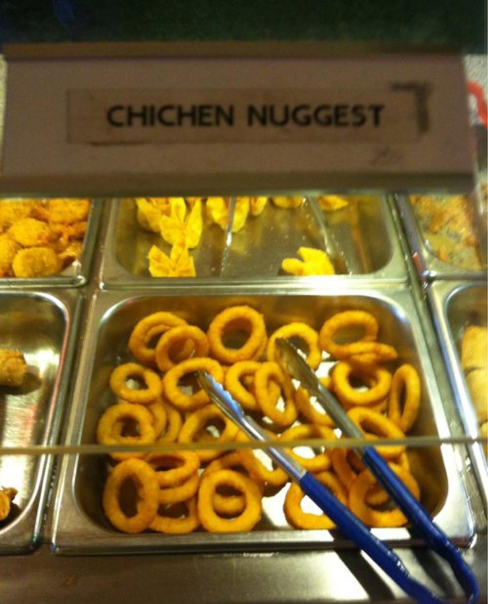 A buffet tray filled with onion rings under a sign that reads "CHICHEN NUGGEST."