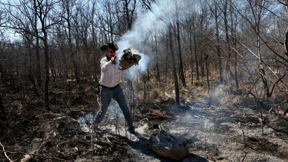 Sammy Schafer tosses a smoldering log into an area already burned after a massive wildfire ripped through the area near Canadian, Texas, on March 1, 2024. - Leah Millis/Reuters