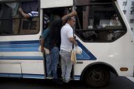 En esta imagen, tomada el 17 de marzo de 2017, un hombre se cuelga de la puerta de un autobús con una bolsa con pan en la mano, en el exterior de una panadería en Caracas, Venezuela. El vicepresidente Tareck El Aissami anunció que las panaderías debían disponer 90% de la harina para producir pan largo, conocido como "canilla", y que el resto podía utilizarse para la elaboración de dulces y panes rellenos. Asimismo ordenó que la venta de pan debía comenzar a las 7 de la mañana. (AP Foto/Fernando Llano)