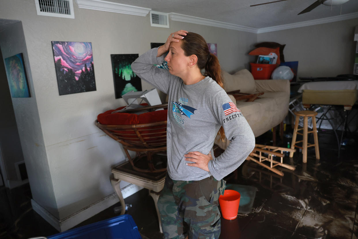 A woman standing with one hand on her hip and the other hand on her forehead stands while she inspects the damage in her flooded apartment.