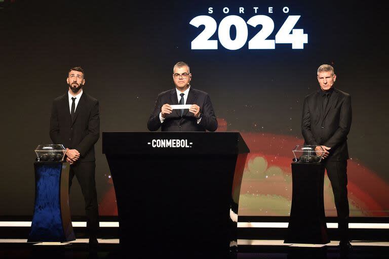 El Director de Competiciones de Clubes de Conmebol, Frederico Nantes, muestra el papel con el nombre de uno de los clubes junto a Lucas Pratto y Martín Palermo, durante el sorteo de la Copa Libertadores