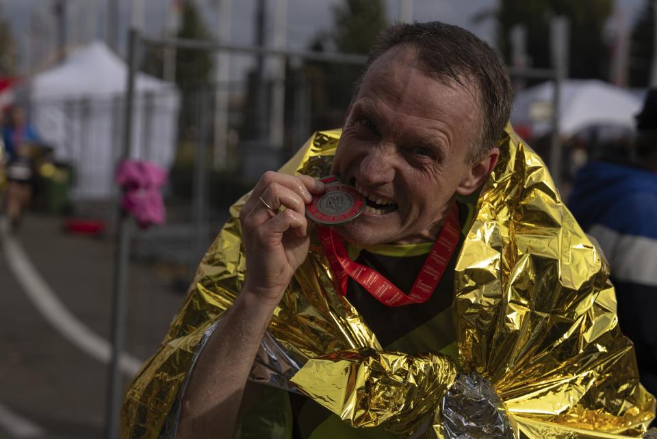 A man bites his medal after finishing the race in Kyiv, Ukraine, Sunday, Oct. 29, 2023. Around two thousand Ukrainians registered for the event, called 'The World's Longest Marathon', with the dual purpose of honoring the country's military and raising funds to bolster Ukraine's air defense system. (AP Photo/Alex Babenko)