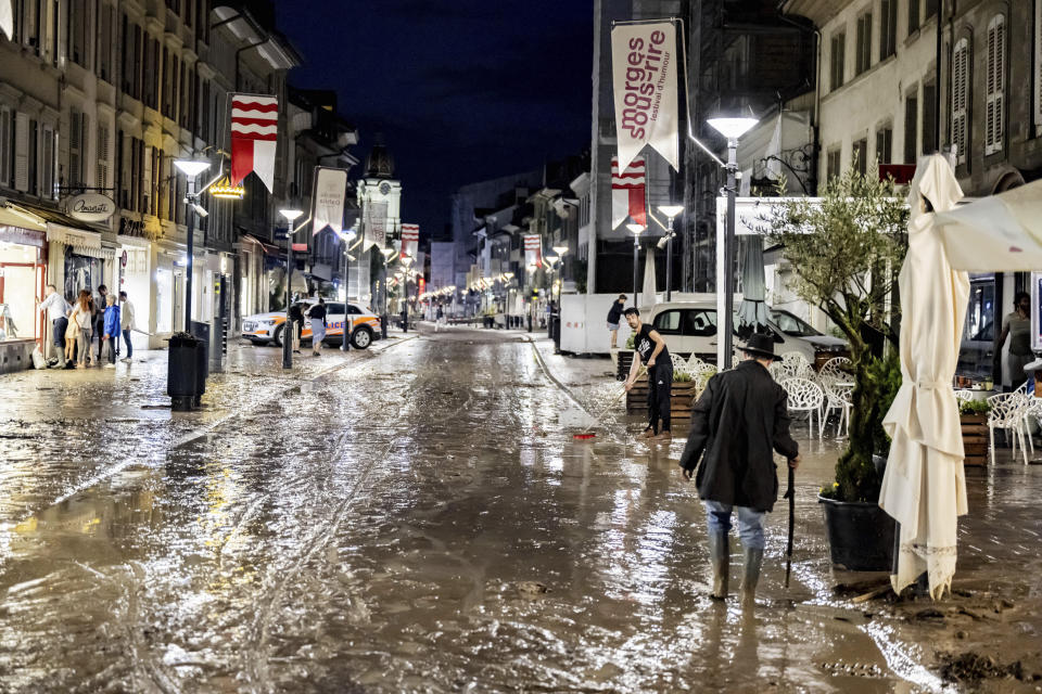 People clear mud from the flooded Grand-Rue following a storm that caused extensive flooding in the town centre on Tuesday 25 June 2024 in Morges, Switzerland. Clean-up crews and business owners were inspecting the damage Wednesday after sudden storms lashed southwestern Switzerland the previous night, sending torrents of water through roads and temporarily halting air traffic at Geneva's airport. In the lakeside town of Morges, a creek overflowed, inundating downtown streets with tan-colored floodwater.(KEYSTONE/Laurent Gillieron)/Keystone via AP)