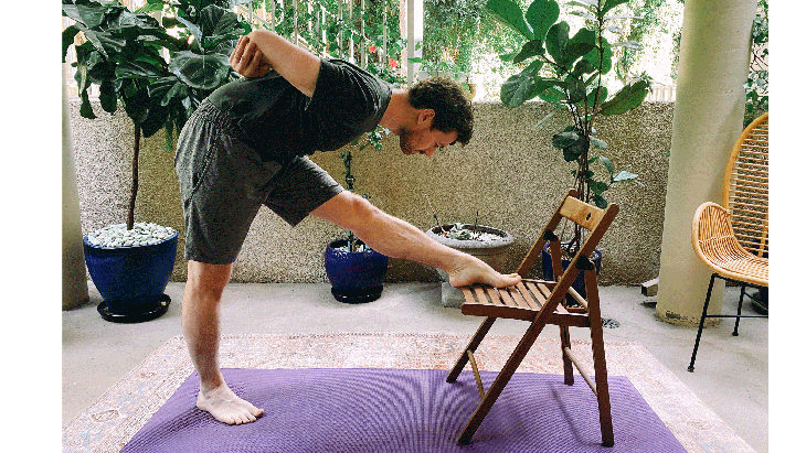 Man standing in front of a chair practicing Pyramid Pose in yoga